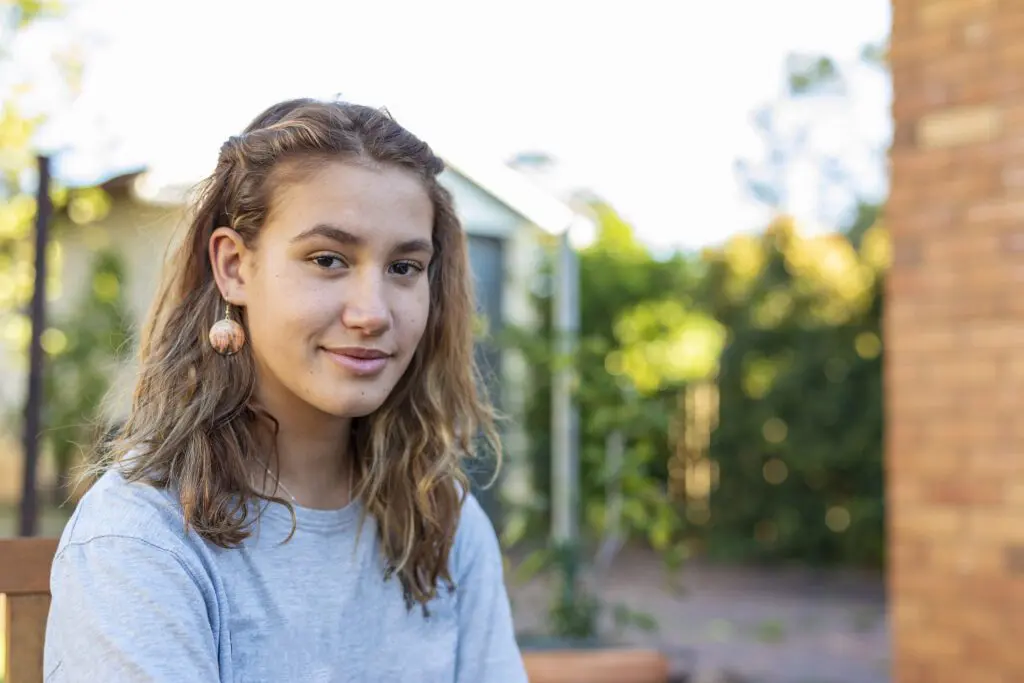 A teenage girl smiles as she stands in a garden outdoors
