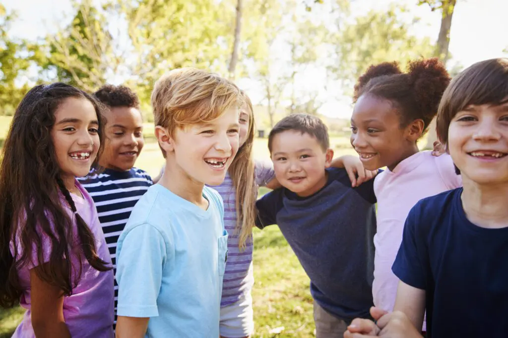 Multi-ethnic group of schoolchildren on a school trip A group of children smile and hug one another in the park