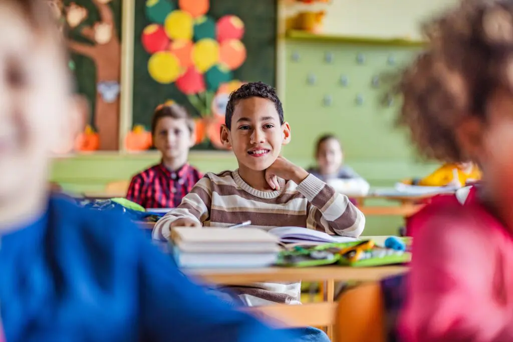 A young boy sits in a colorful classroom with his peers